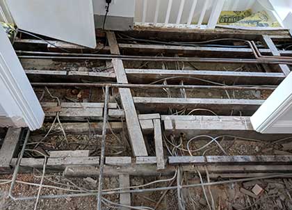 Removing the old pine boards reveals pipes, wires and uneven joists