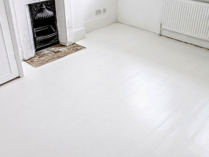 A bright room featuring old pine floorboards painted entirely white, creating a clean look next to an original black cast iron fireplace