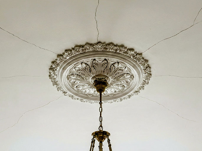 A lath and plaster ceiling showing visible cracks caused by vibration from nail punching on the pine floorboards above