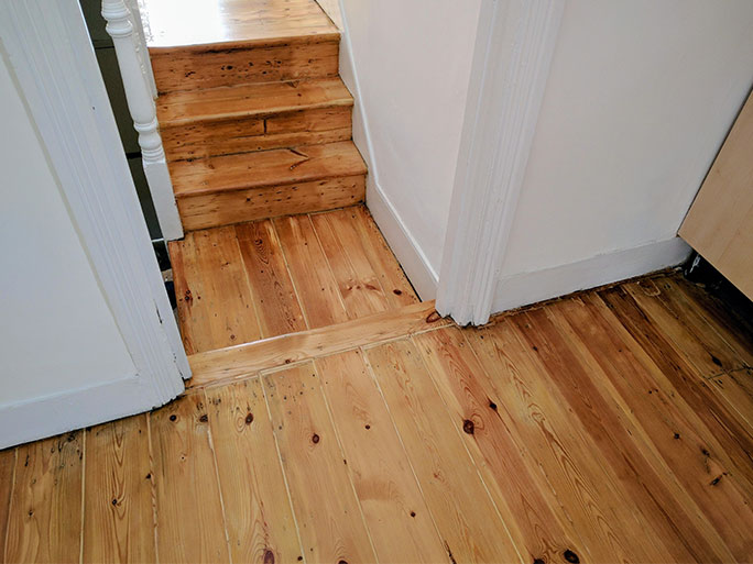 A renovated rustic look pine victorian floor with gaps filled with pine slivers, in the hallway with the steps, oiled clear satin