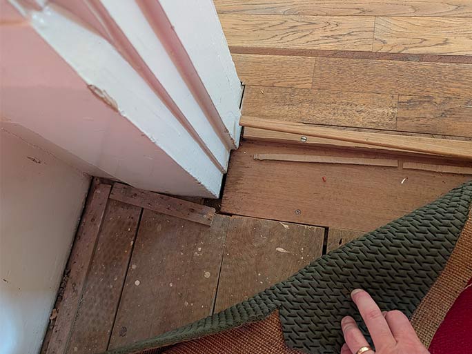 Hand lifting a carpet and underlay at a threshold to reveal the underlying subfloor boards during an initial site survey #CraftedForLife