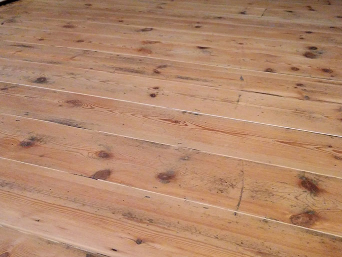Close-up of sanded pine floorboards showing natural imperfections, dark wood knots, grain variations, and deeply embedded marks that cannot be completely removed