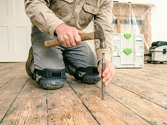 Flooring specialist carries out nail punching to counter-sink clasp nail heads below the surface of pine floorboards before sanding; this can cause vibration in the ceiling below