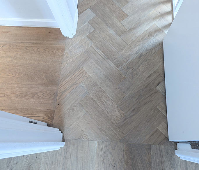 Oak herringbone and straight planks matched in tone at a doorway #CraftedForLife