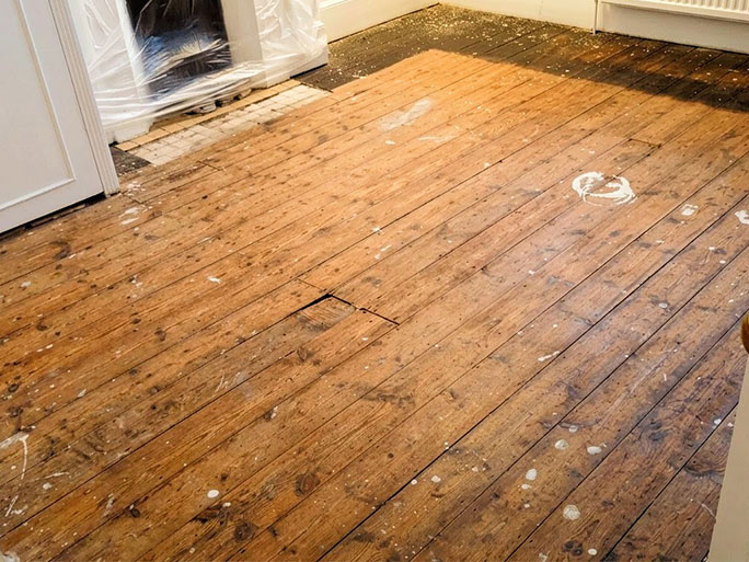 Old pine floorboards before restoration showing dark black bitumen or tar stains around the edges of the room at the ends of the boards.