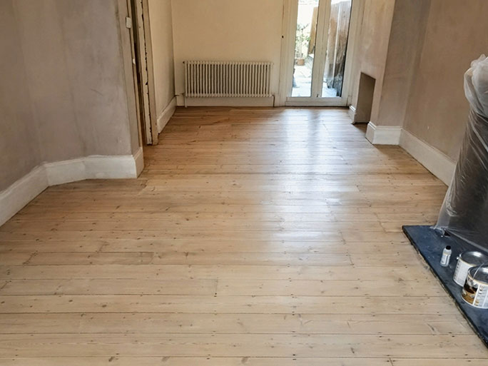 Restored pine floorboards sealed with white wood oil, allowing the natural wood grain and knots to remain subtly visible across the room