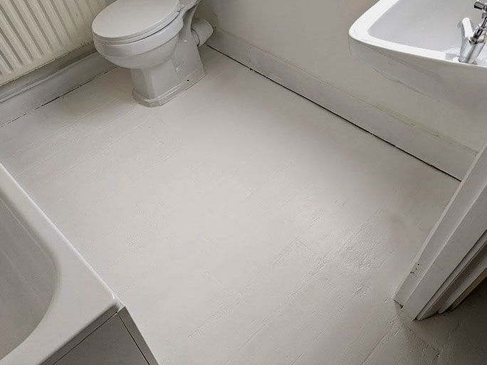 The completed bathroom floor restoration, showing the original pine floorboards painted with a solid, clean coat of white floor paint